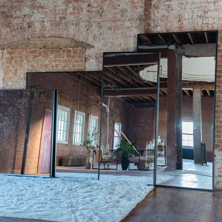 Large wall mount mirrors reflecting a room with brick walls and modern decor.