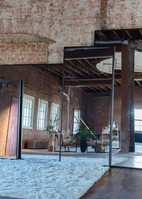 Large wall mount mirrors reflecting a room with brick walls and modern decor.