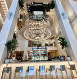 Modern restaurant interior with a large chandelier, LiteMirror ceiling tiles, bar area, and chairs.