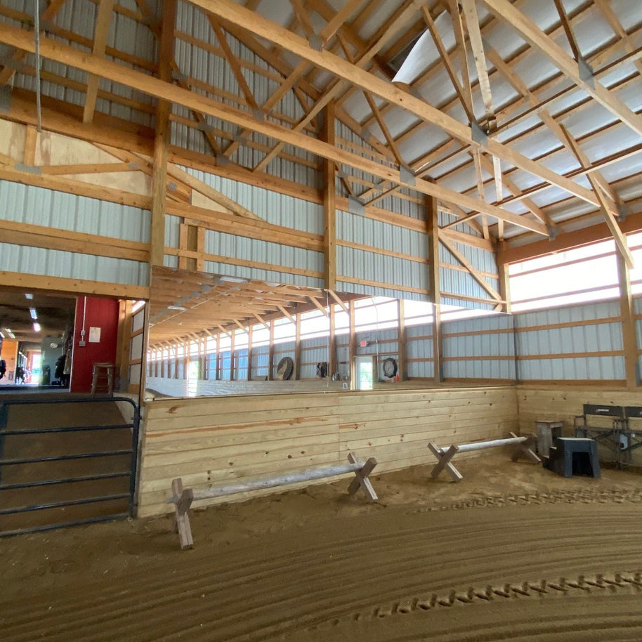 Interior of a wooden indoor riding arena with benches and mirrors.