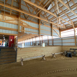 Interior of a wooden indoor riding arena with benches and mirrors.