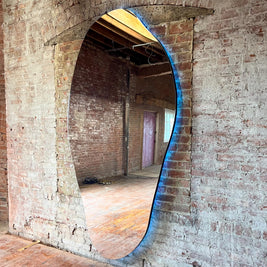 Large oval mirror illuminated from the back mounted on a brick wall