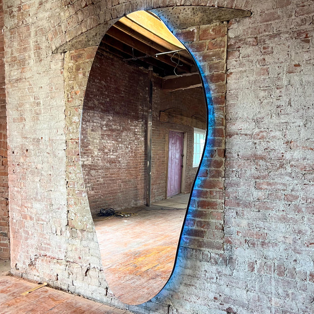 Large oval mirror illuminated from the back mounted on a brick wall