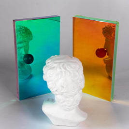 White ceramic head sculpture in front of two colorful mirror panels. 