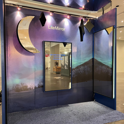 Display of LiteMirror product with aurora borealis and mountain range backdrop in a trade show booth setting