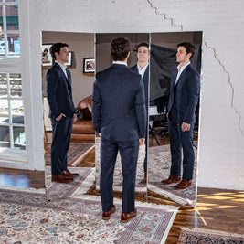 Male model in front of three panel mirror in front of white brick wall. 