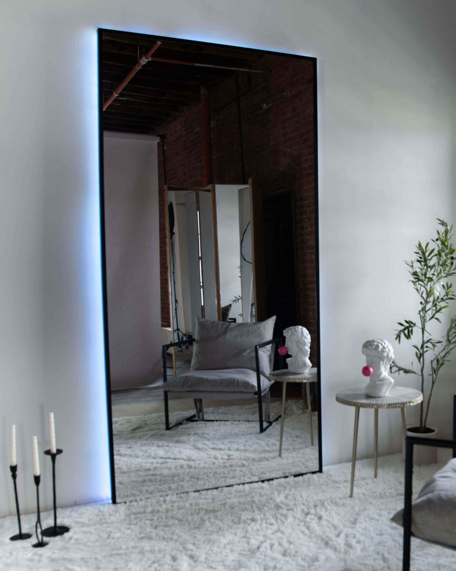 Wall mount mirror with black wood frame and white back light in a living room setting