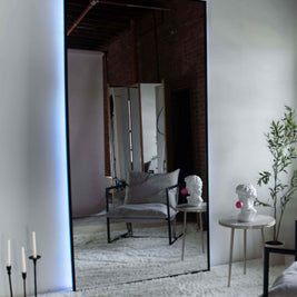 Wall mount mirror with black wood frame and white back light in a living room setting