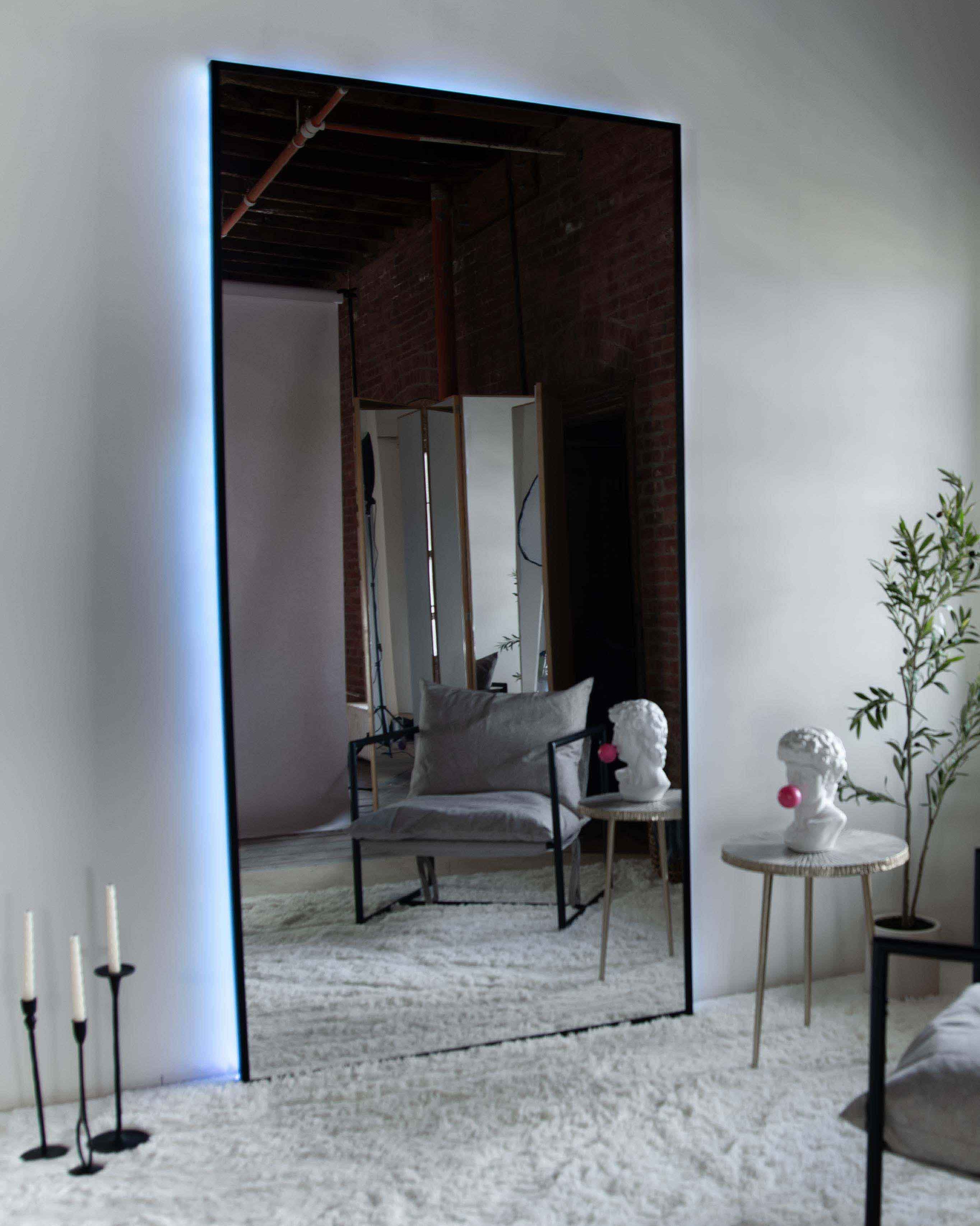 Wall mount mirror with black wood frame and white back light in a living room setting