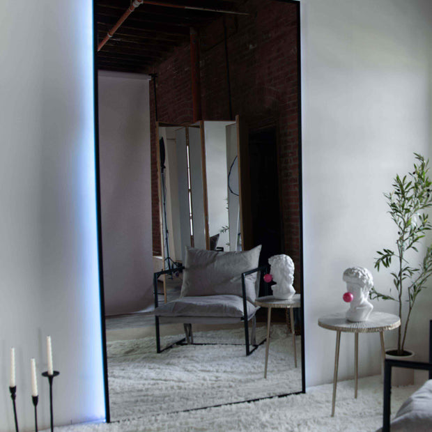 Wall mount mirror with black wood frame and white back light in a living room setting