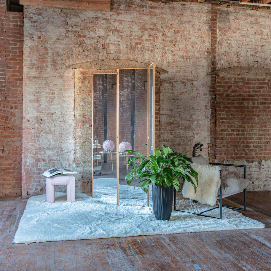 Four-paneled mirror staged as a room divider in a modern interior with brick walls, wooden floor, and decorative elements.