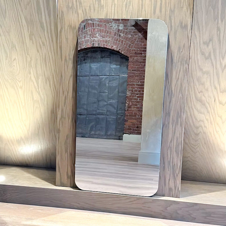 Rectangular mirror with wooden frame leaning against a wooden wall.