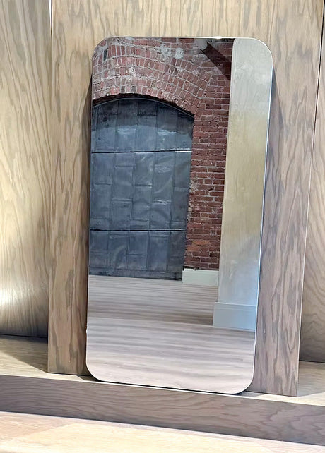 Rectangular mirror with wooden frame leaning against a wooden wall.