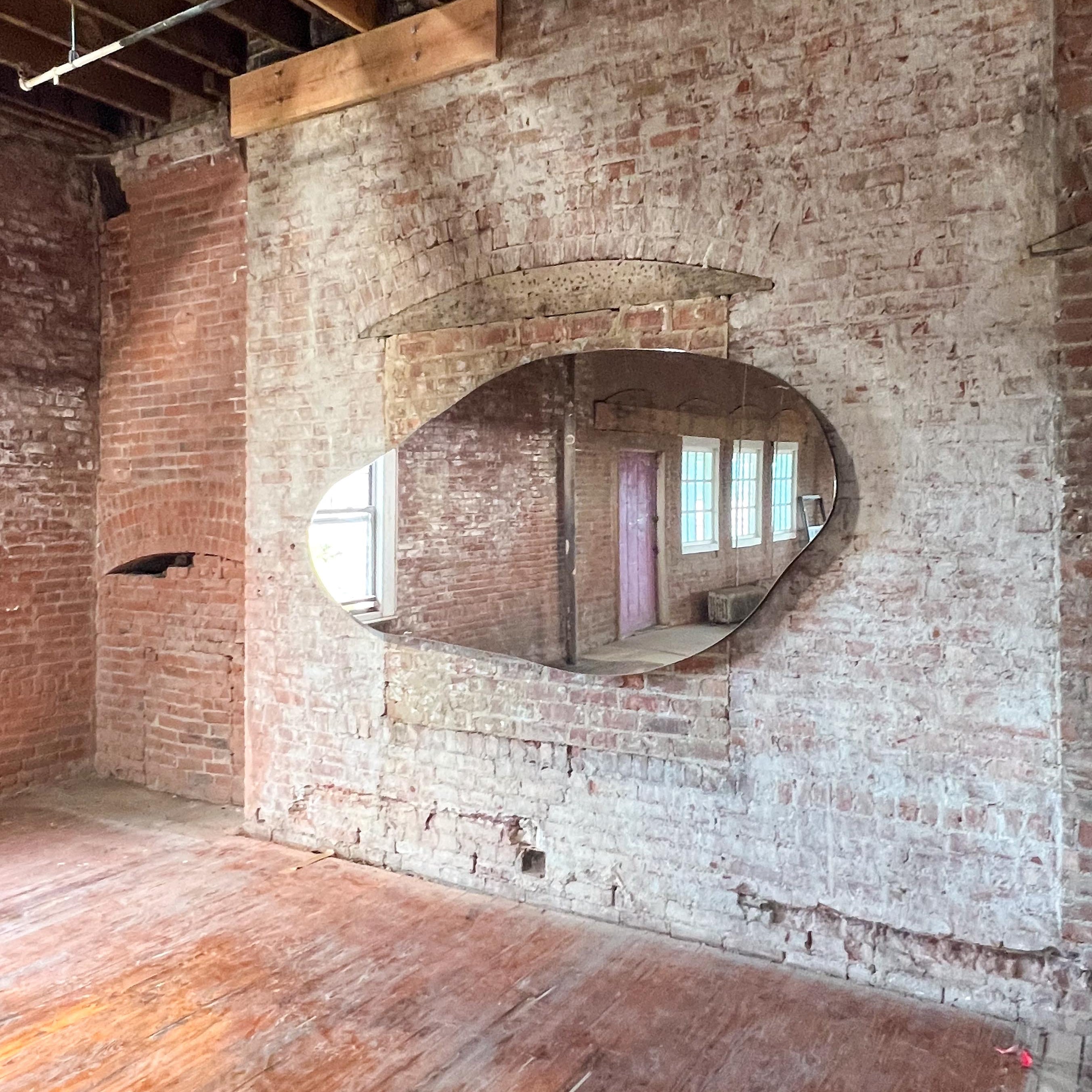 Brick wall with a large oval mirror reflecting a window