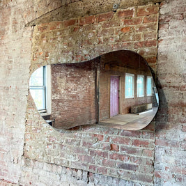 Rounded asymmetrical mirror embedded in a brick wall