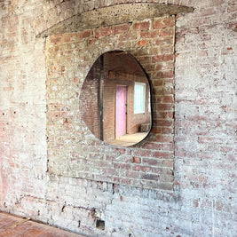 Small asymmetrical mirror on a brick wall with a view of a pink door.