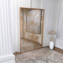Gold antiqued mirror with textured surface  and wood frame in a room with white walls and a rug.