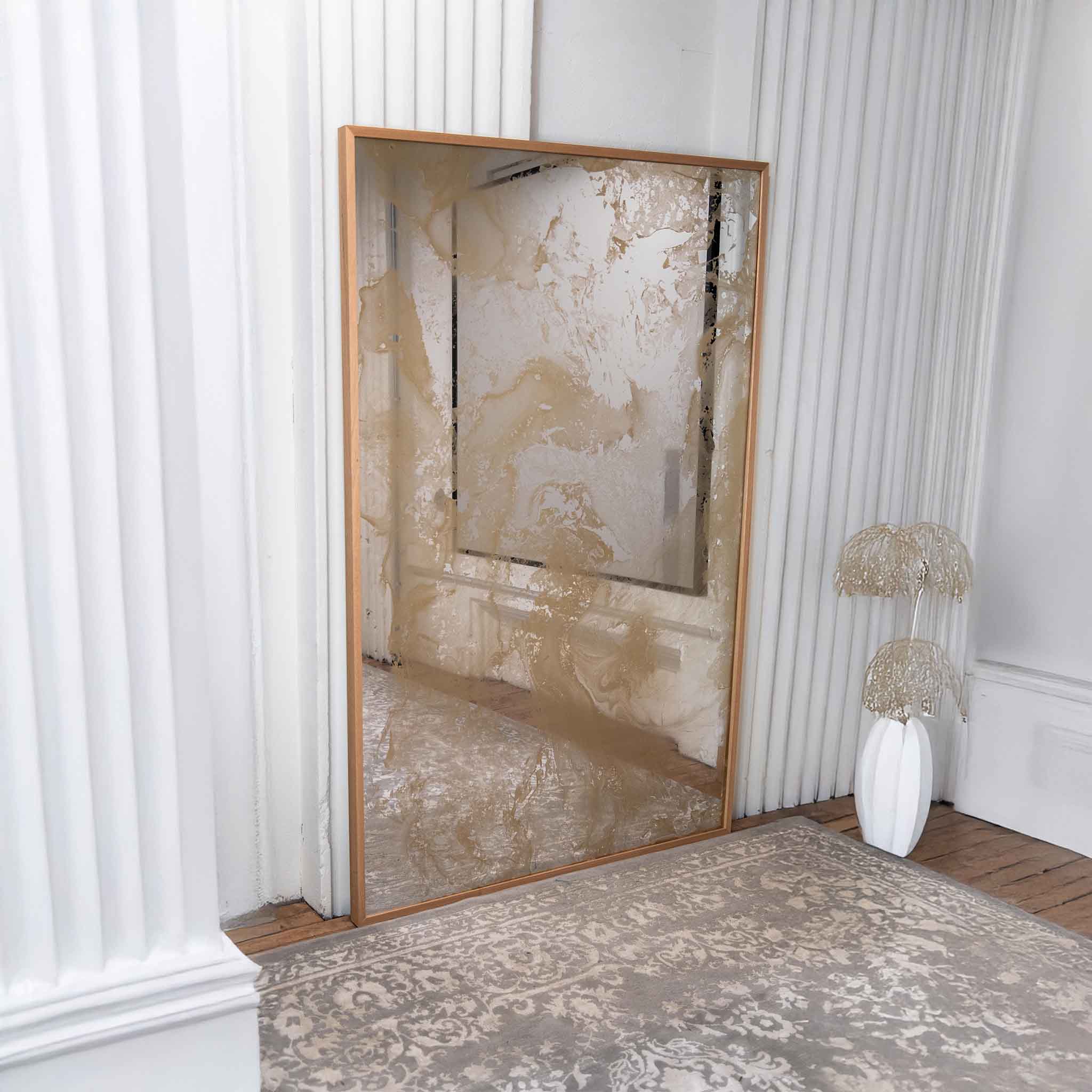 Gold antiqued mirror with textured surface  and wood frame in a room with white walls and a rug.