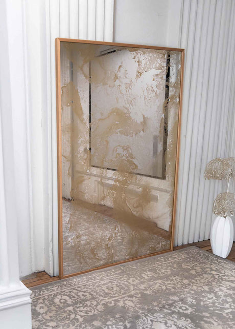 Gold antiqued mirror with textured surface  and wood frame in a room with white walls and a rug.
